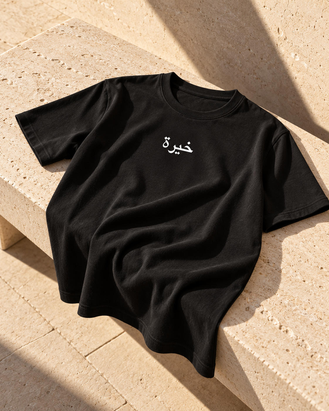 KHIRAH black tee in warm light on a stone bench